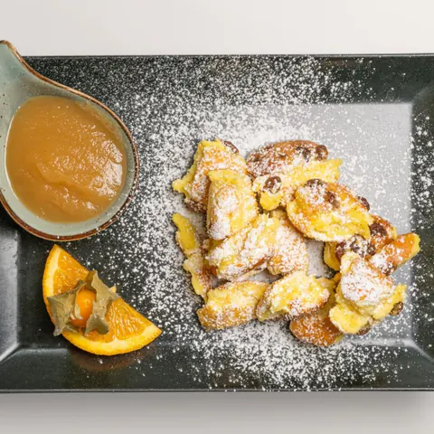 Kaiserschmarrn with icing sugar, apple sauce and fresh orange